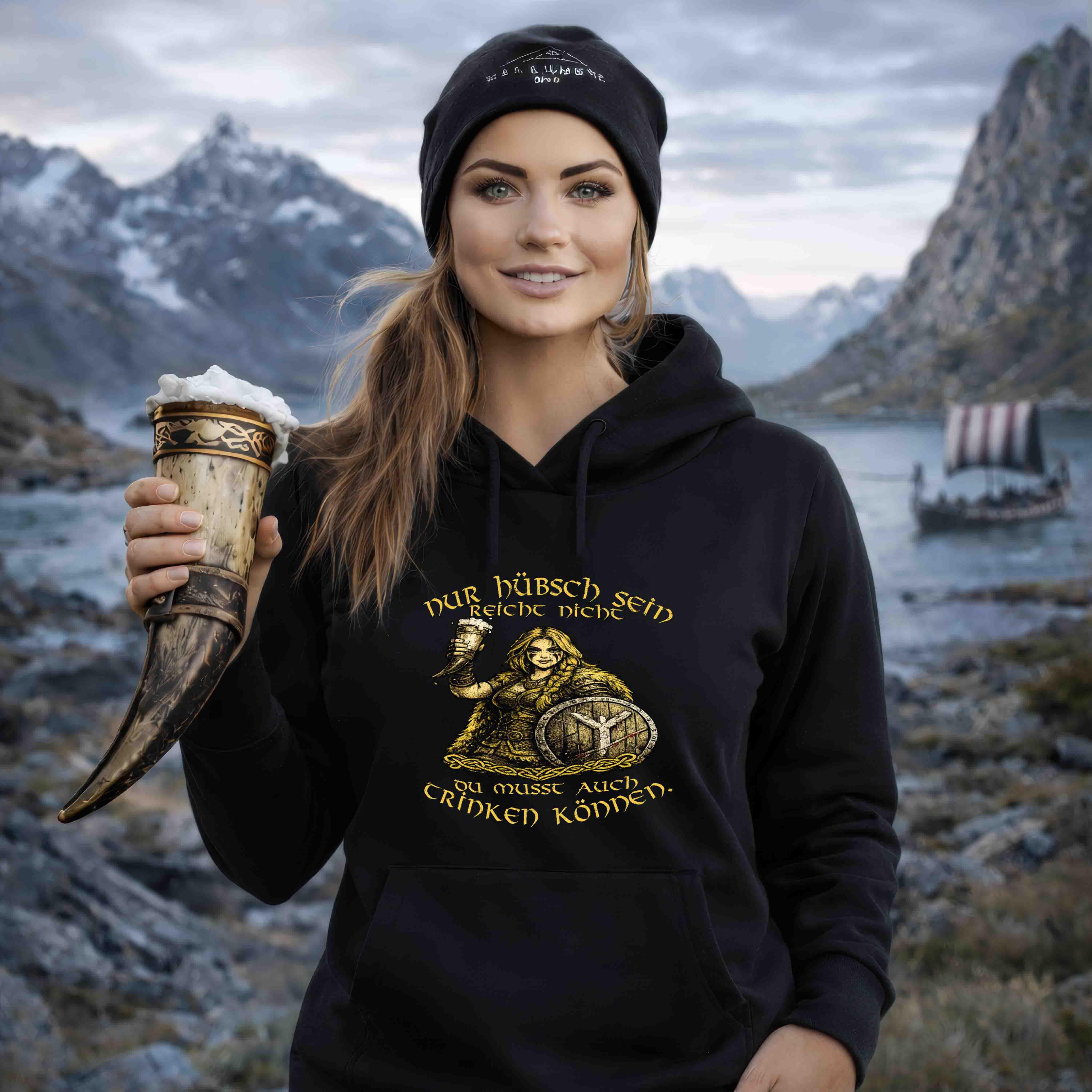 Frau in Wikinger Hoodie mit Trinkhorn vor nordischer Fjordlandschaft, Wikingerschiff im Hintergrund.