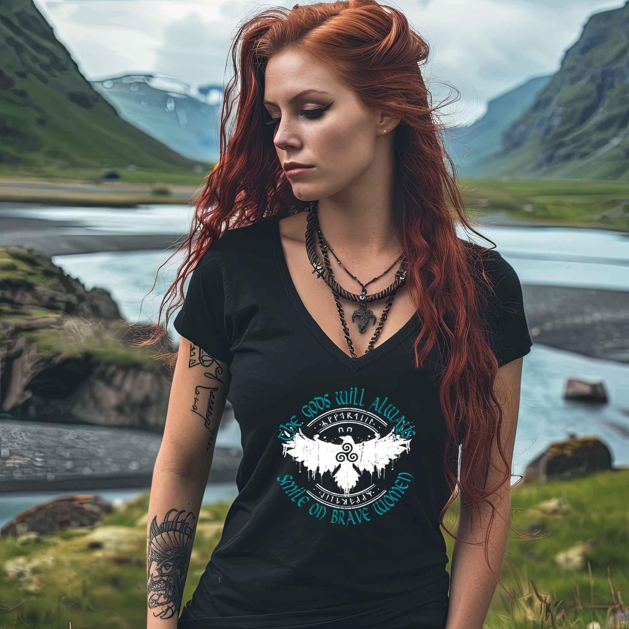 Woman wearing Schildmaiden V-Neck shirt with "The Gods Will Always Smile on Brave Women" design featuring a Triskelion and eagle in nature setting