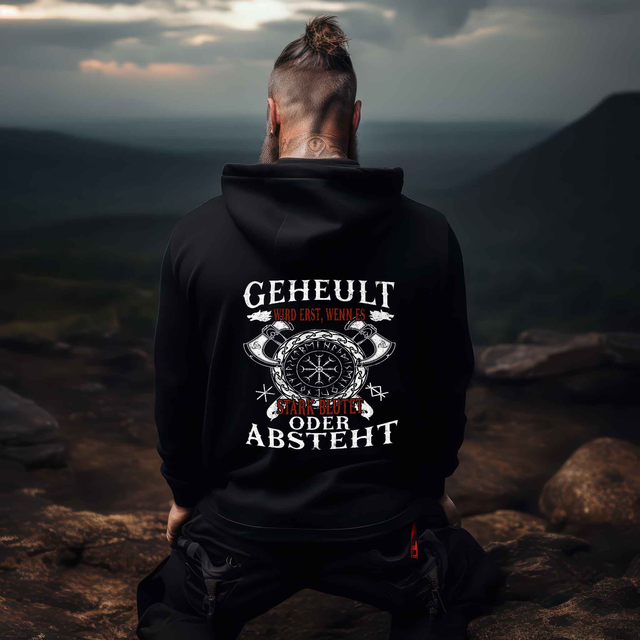 Person wearing Lustiger Wikinger Hoodie with Helm of Awe design and humorous text, sitting outdoors with mountain backdrop.