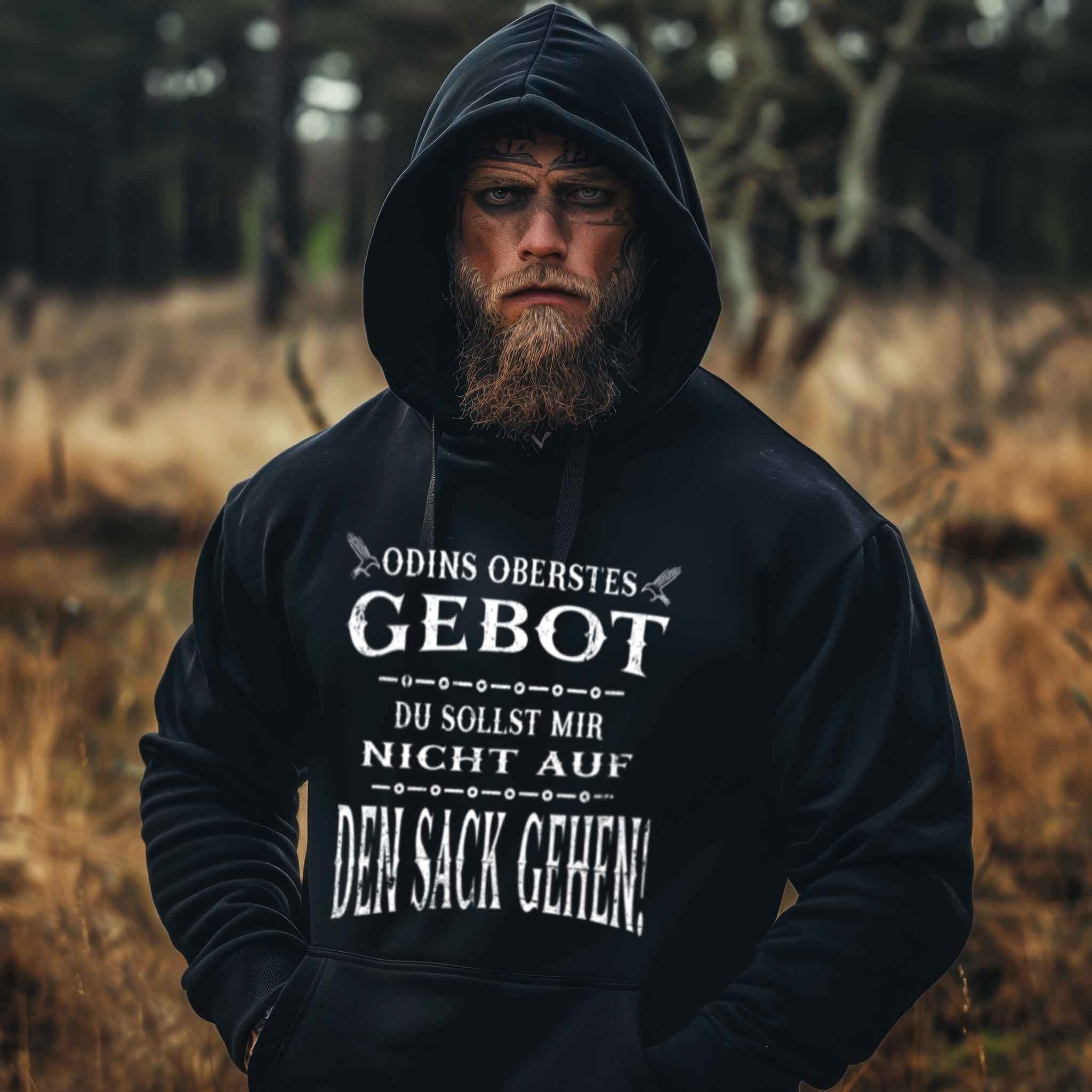 Bearded man wearing "Odins Oberstes Gebot: Du Sollst Mir Nicht Auf Den Sack Gehen!" Viking oversized hoodie in a forest.