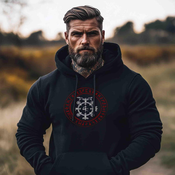Mann mit Bart trägt schwarzen Wikinger-Hoodie mit Runen und nordischem Symbol, draußen im Freien.