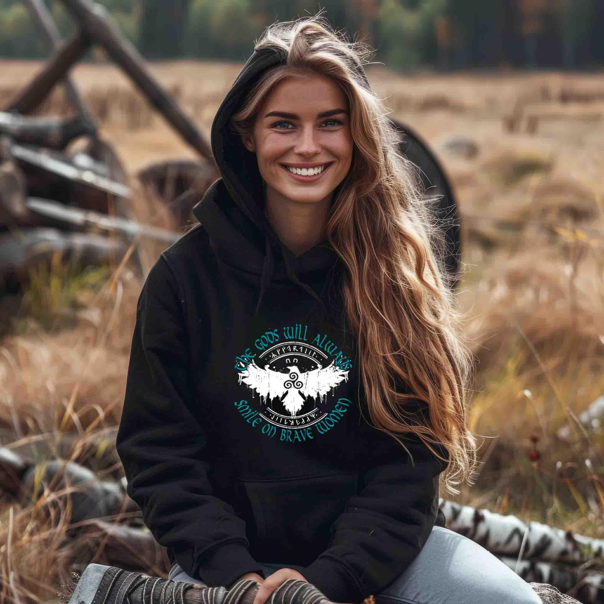 Woman wearing Schildmaiden Hoodie with "The Gods Will Always Smile on Brave Women" text, featuring Celtic Triskelion and stylized eagle design