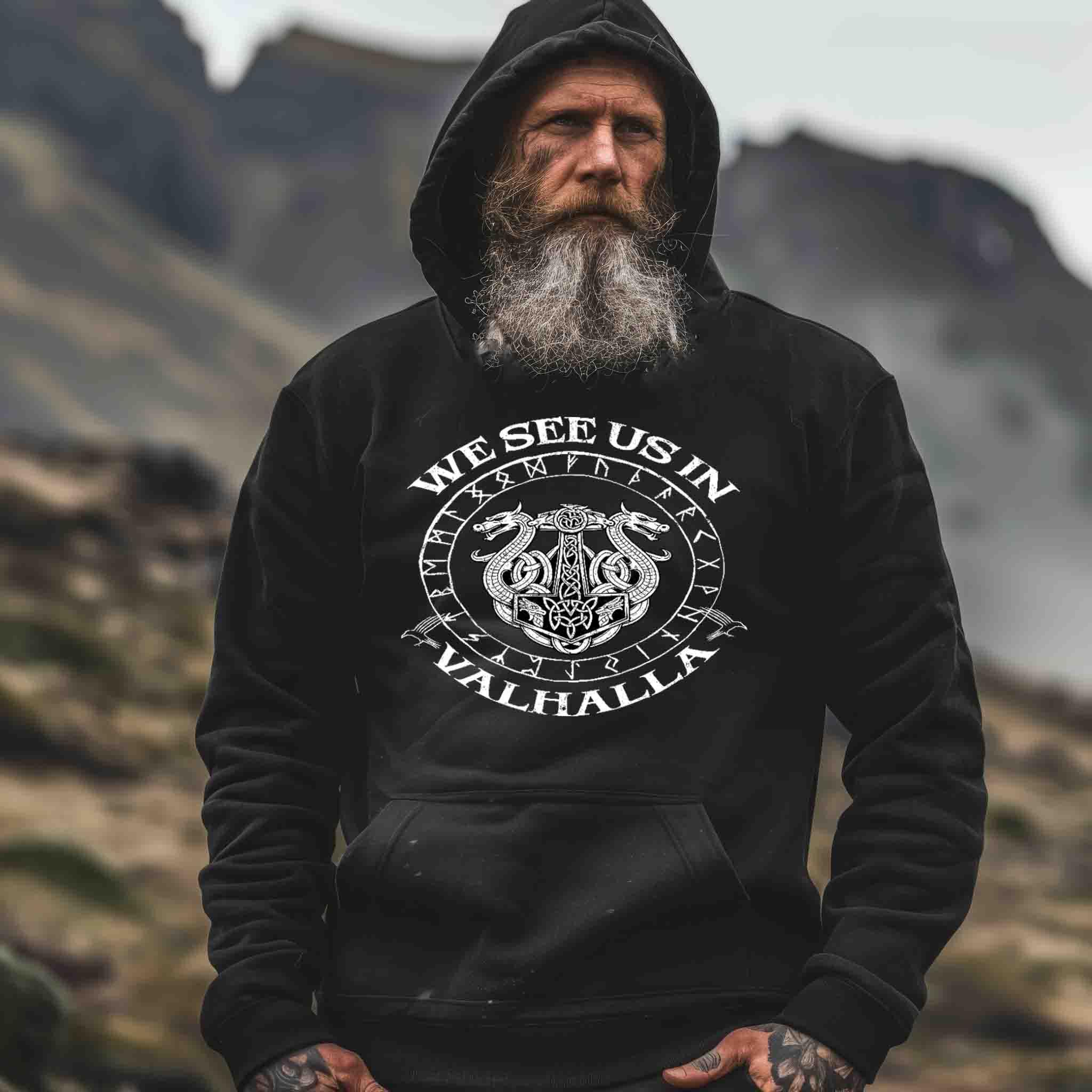 Mann mit langem Bart im Wikinger-Hoodie mit Valhalla-Motiv vor nordischer Landschaft