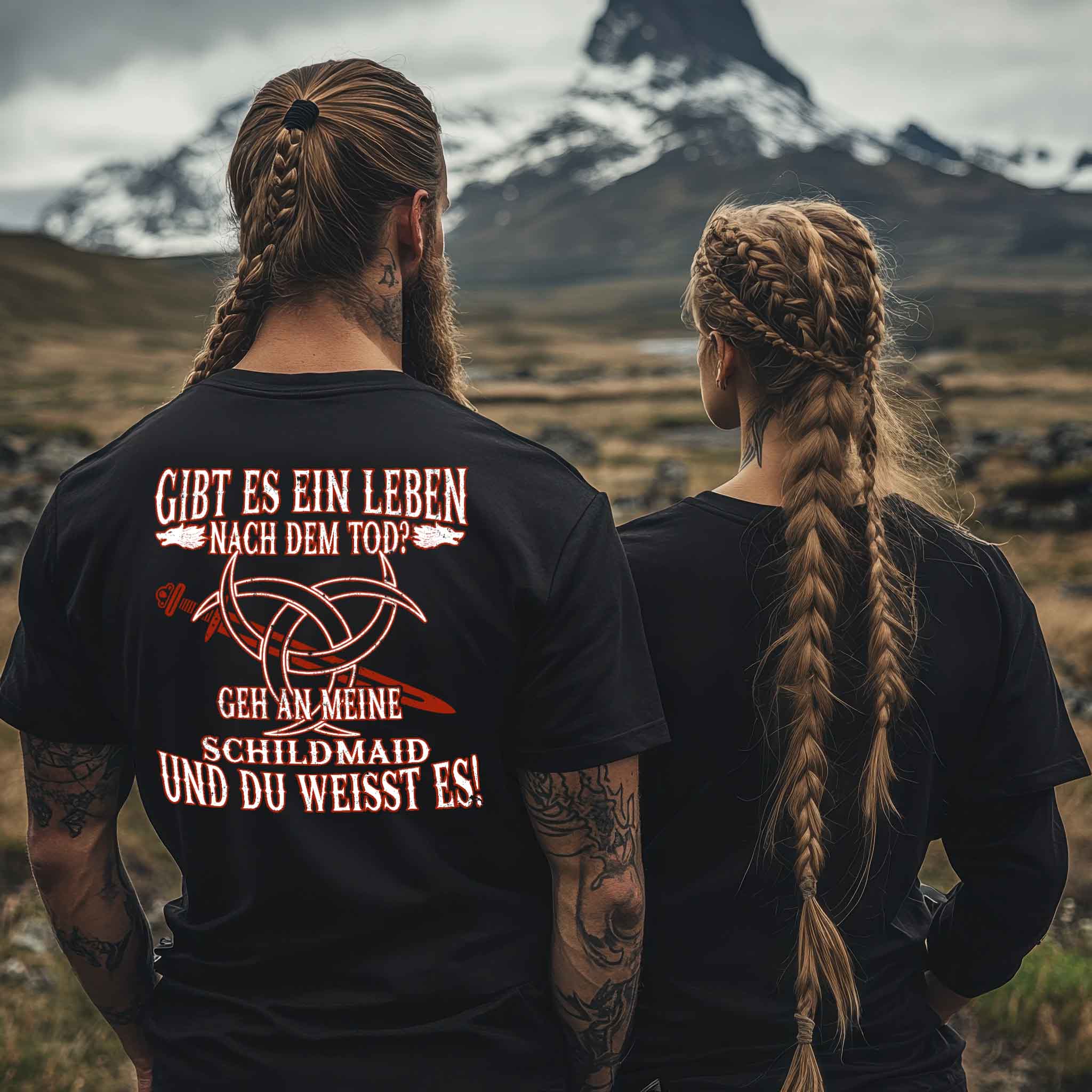 Viking couple wearing "Gibt es ein Leben nach dem Tod? Geh an meine Schildmaid und du weißt es!" shirt with Nordic symbols and mountain background