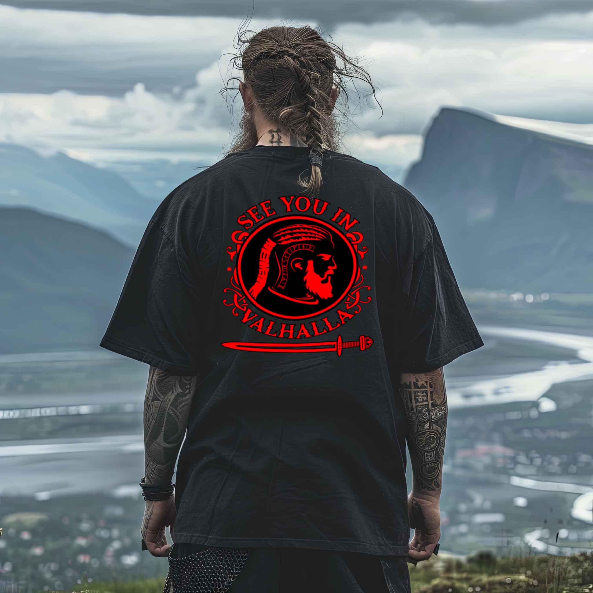 Viking enthusiast wearing oversized "See You In Valhalla" shirt with warrior profile, runes, and sword design, overlooking a scenic Nordic landscape